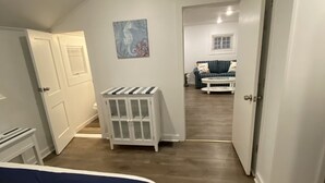 Ein Schlafzimmer mit einem Bett, einem weißen Schrank, einem Gemälde und einem Flur, der in einen Wohnbereich mit einer Couch und einem Couchtisch führt.