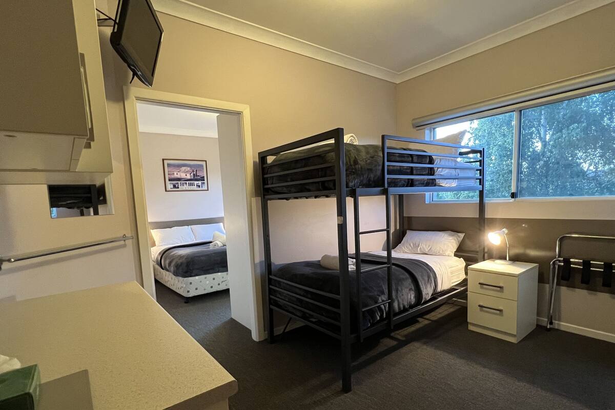 A compact room with bunk beds, a small desk, a window with a view, and a television mounted on the wall.