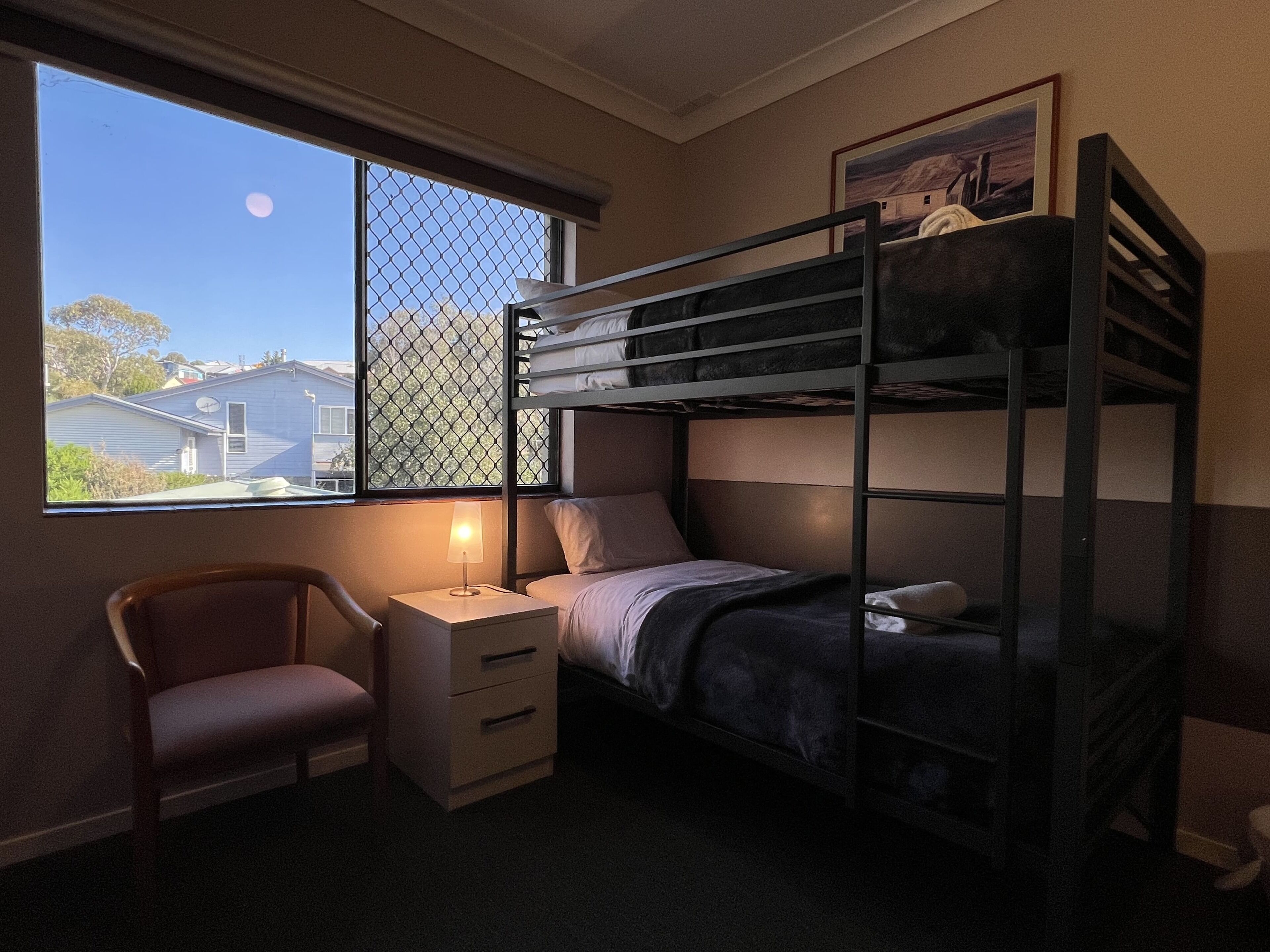 A bunk bed room with a desk, chair, and a window with a view of houses and a moon.