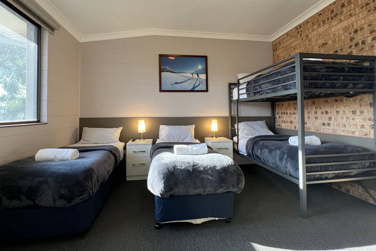 A room with two single beds, a bunk bed, and a desk with a lamp.