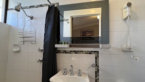 A bathroom with a shower, a sink, a towel rack, a toilet paper holder, and a hairdryer.