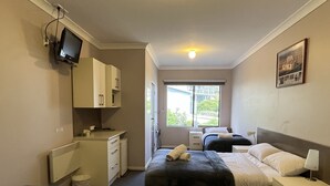 A hotel room with a bed, a desk, a chair, a television, and a window.