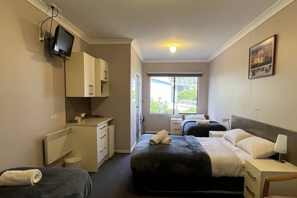 A hotel room with a bed, a desk, a chair, a television, and a window.