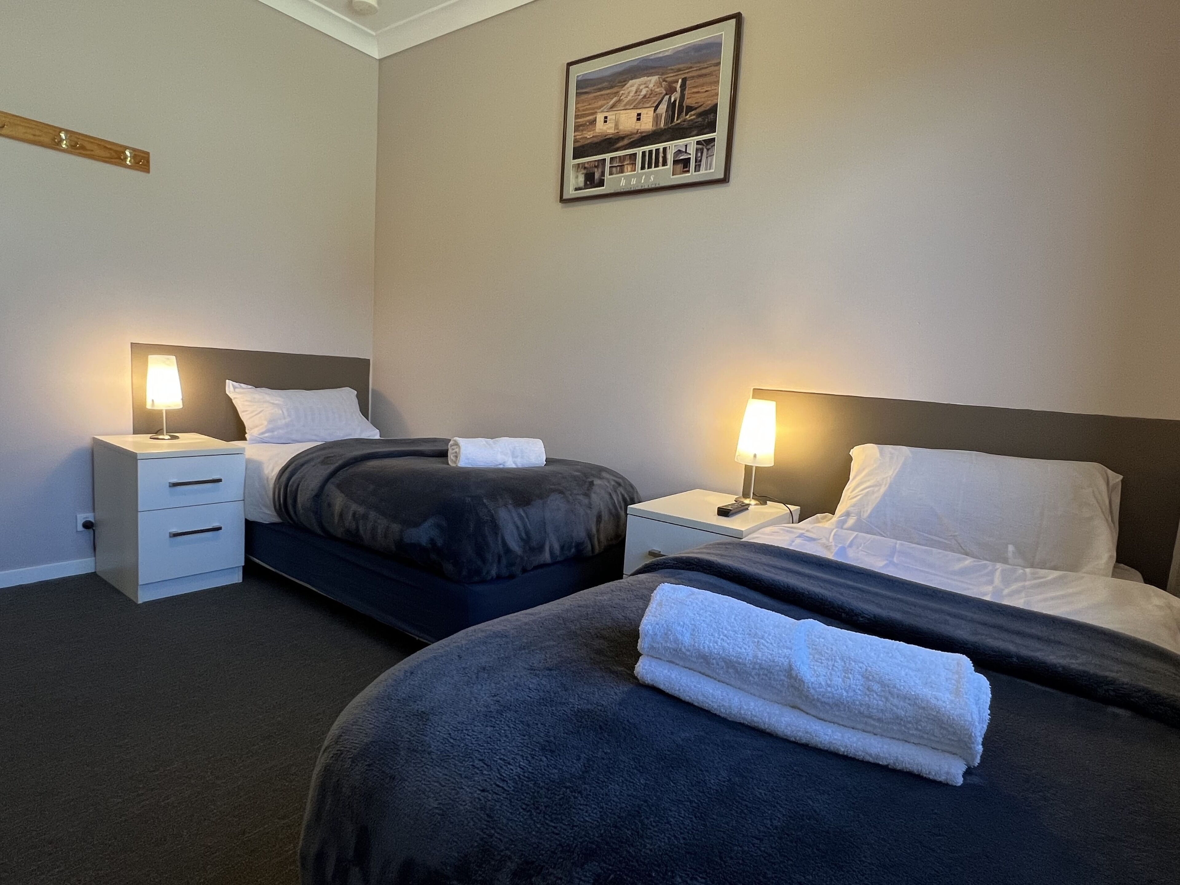 Habitación de hotel con dos camas, cada una con una mesita de noche y una lámpara. Hay un cuadro enmarcado en la pared sobre las camas.