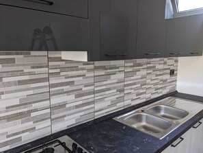 Una cocina moderna con encimera negra, pileta de acero inoxidable y muebles grises.