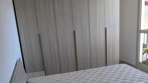 Quarto com uma cama de solteiro, um guarda-roupa de madeira e uma janela com vista.