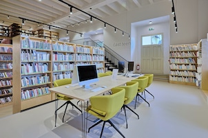 Una biblioteca moderna con estanterías, una computadora y una mesa con sillas.