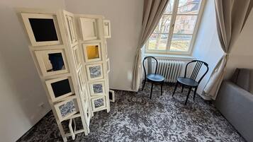 A corner room with a white cabinet with multiple compartments, two black chairs, a radiator, and a window with curtains.