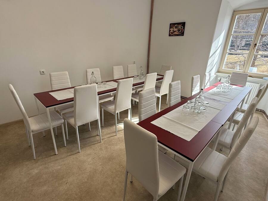 A dining area with a long table, white chairs, and a window with a view of trees.
