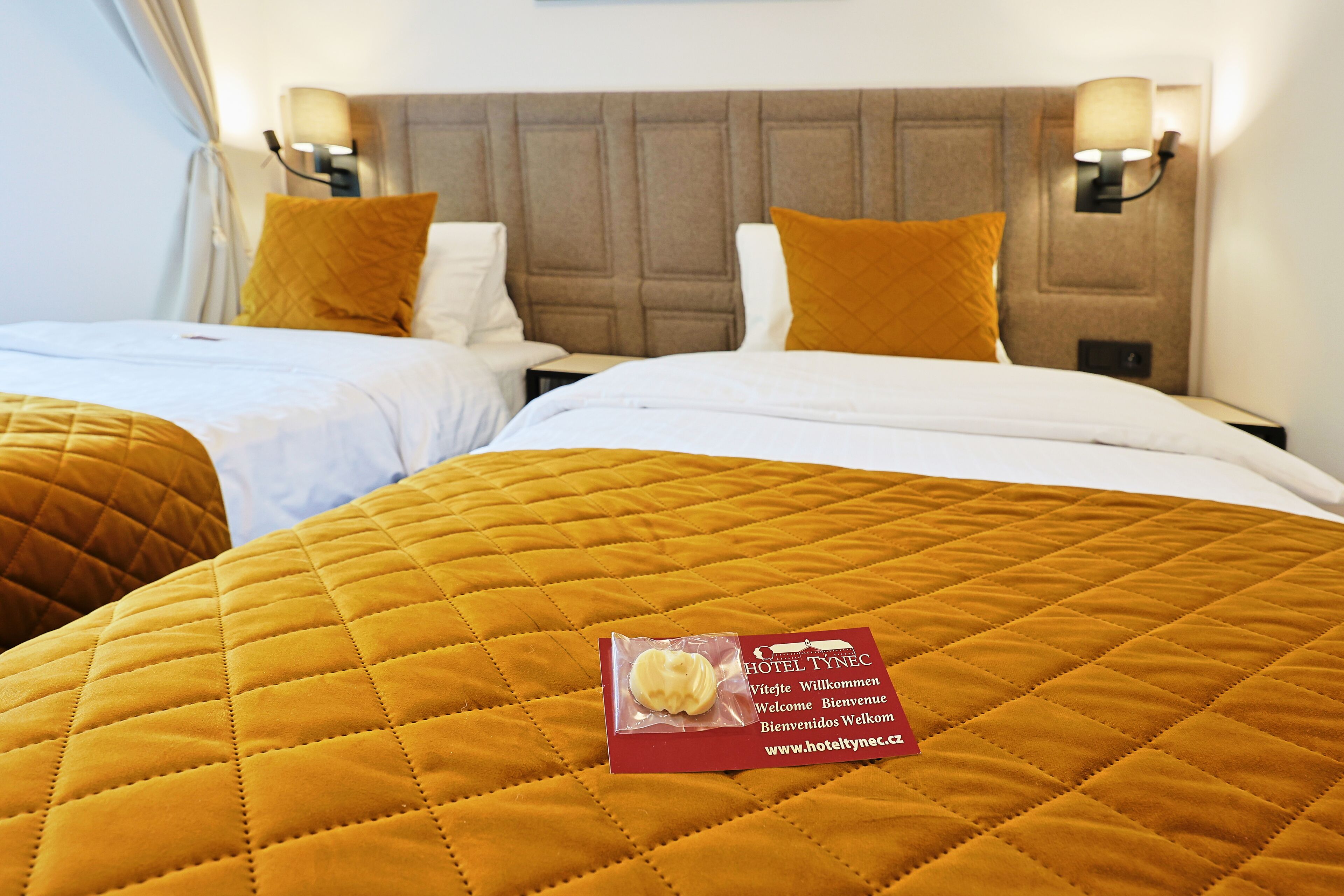 A hotel room with two beds, each with a quilted mattress and pillows. There is a welcome card on the bed.
