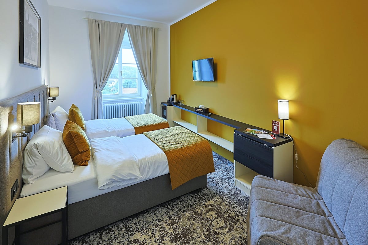 Habitación de hotel con dos camas, un televisor, un escritorio con lámpara y una ventana con cortinas.