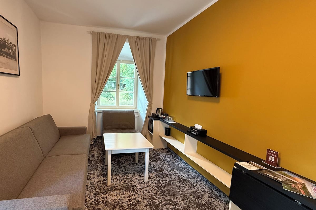 Una habitación moderna con sofá, una mesita, televisión instalada en la pared y ventana con cortinas.