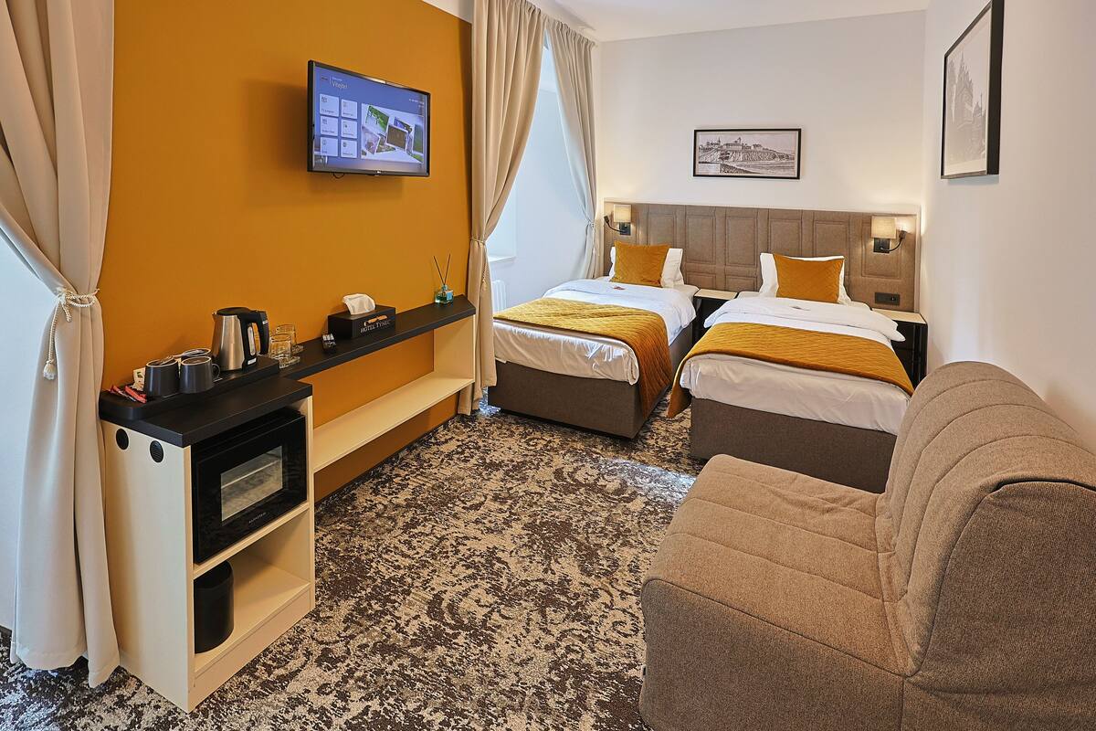 Habitación de hotel con dos camas, un televisor en la pared, un escritorio con hervidor y un sofá.