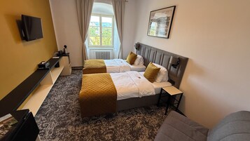 Una habitación de hotel con dos camas, un escritorio, una silla, un televisor y una ventana con cortinas.