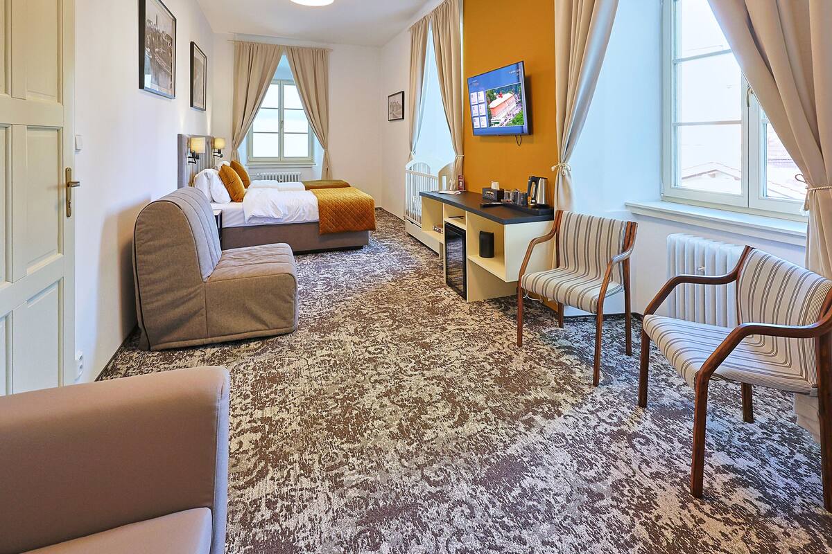 Una habitación de hotel con una cama, un escritorio, dos sillones y una alfombra estampada.