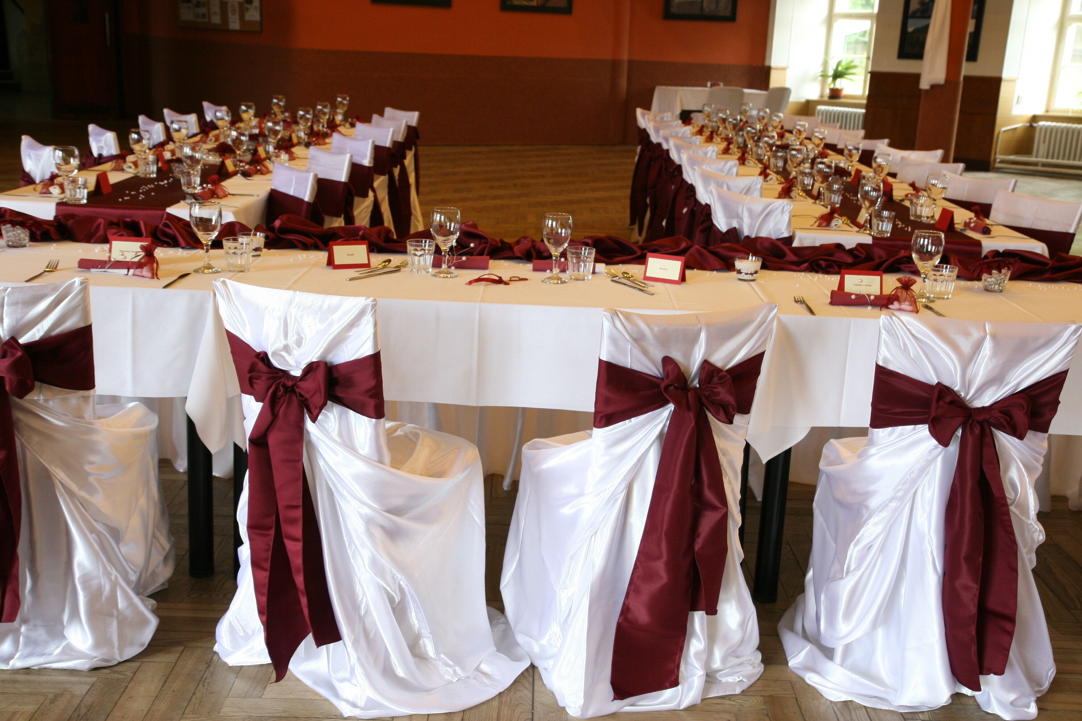 A banquet hall with tables set for a formal event, featuring white tablecloths and red sashes.