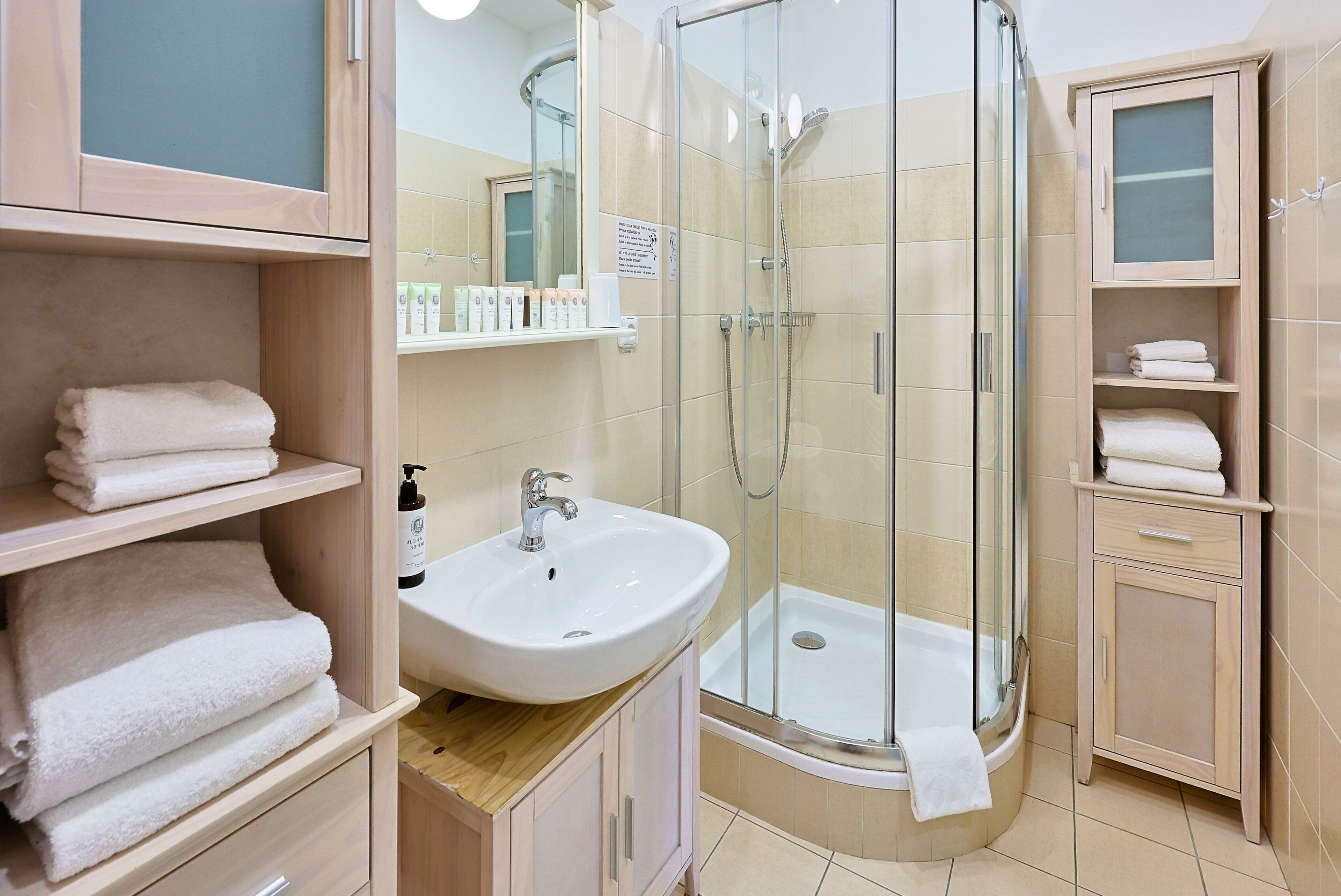 A modern bathroom with a glass-enclosed shower, a sink, and shelves with folded towels.