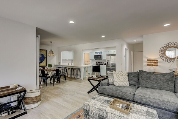 A modern living room with a grey sofa, a coffee table, and a dining area with a wooden table and chairs.