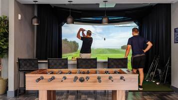 A foosball table in a room with a large screen displaying a golf scene.