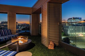 Terraza en la azotea con un brasero, zona de estar y vistas a la ciudad al atardecer.