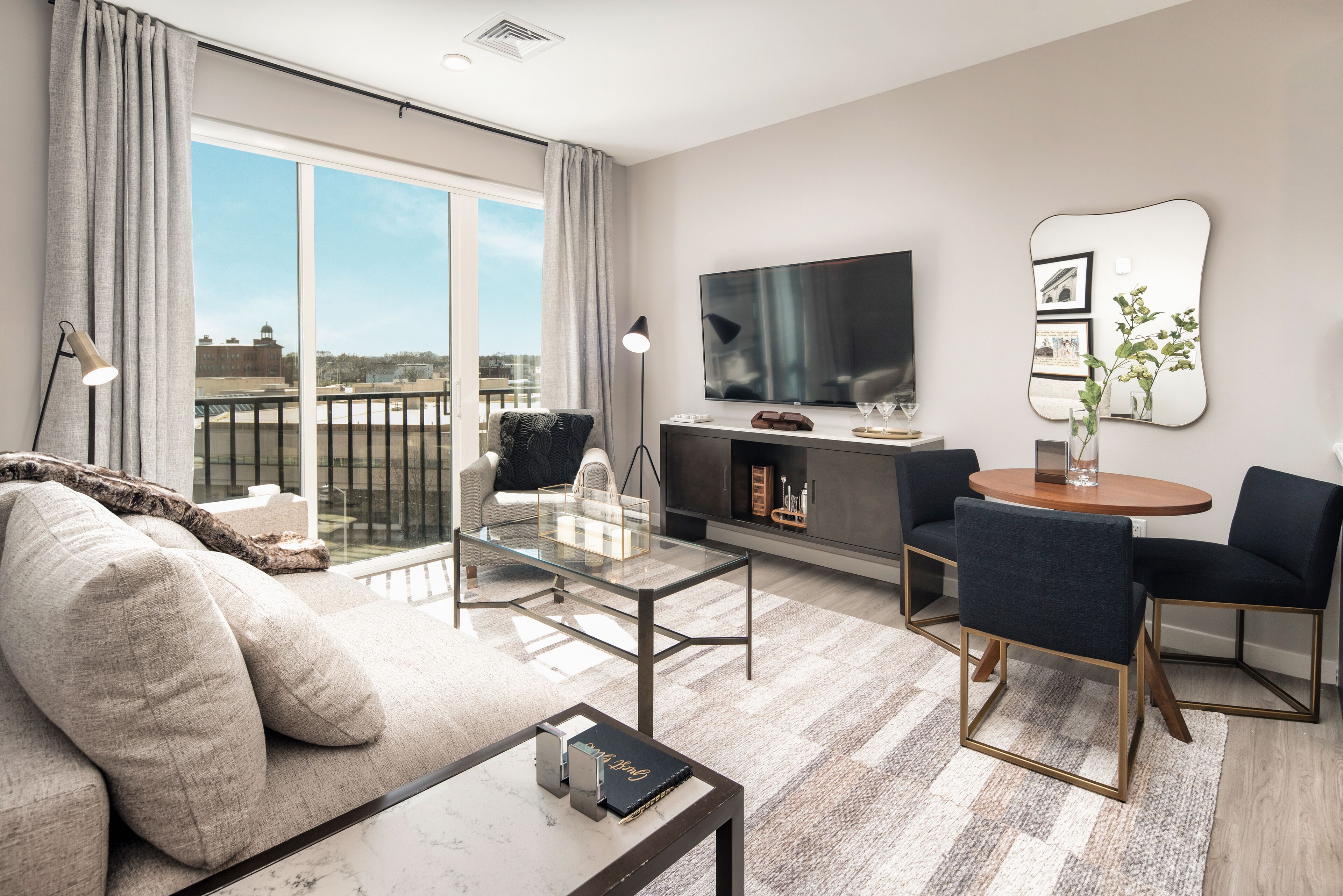 A modern living room with a sofa, a glass coffee table, a TV, and a dining area with chairs and a table.