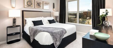 Ein modernes Hotelzimmer mit einem großen Bett, Nachttischen, einem Schreibtisch mit einer Schale und einem Fenster mit Blick.