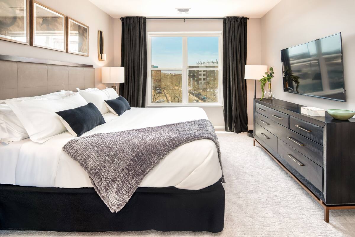 Une chambre d’hôtel moderne avec un grand lit, une commode en bois foncé et un téléviseur à écran plat.