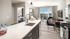 A modern kitchen with a large island, a dining area with a round table, and a view of the outdoors through large windows. - Hyatus Luxury Residences City Crossing (New Haven)