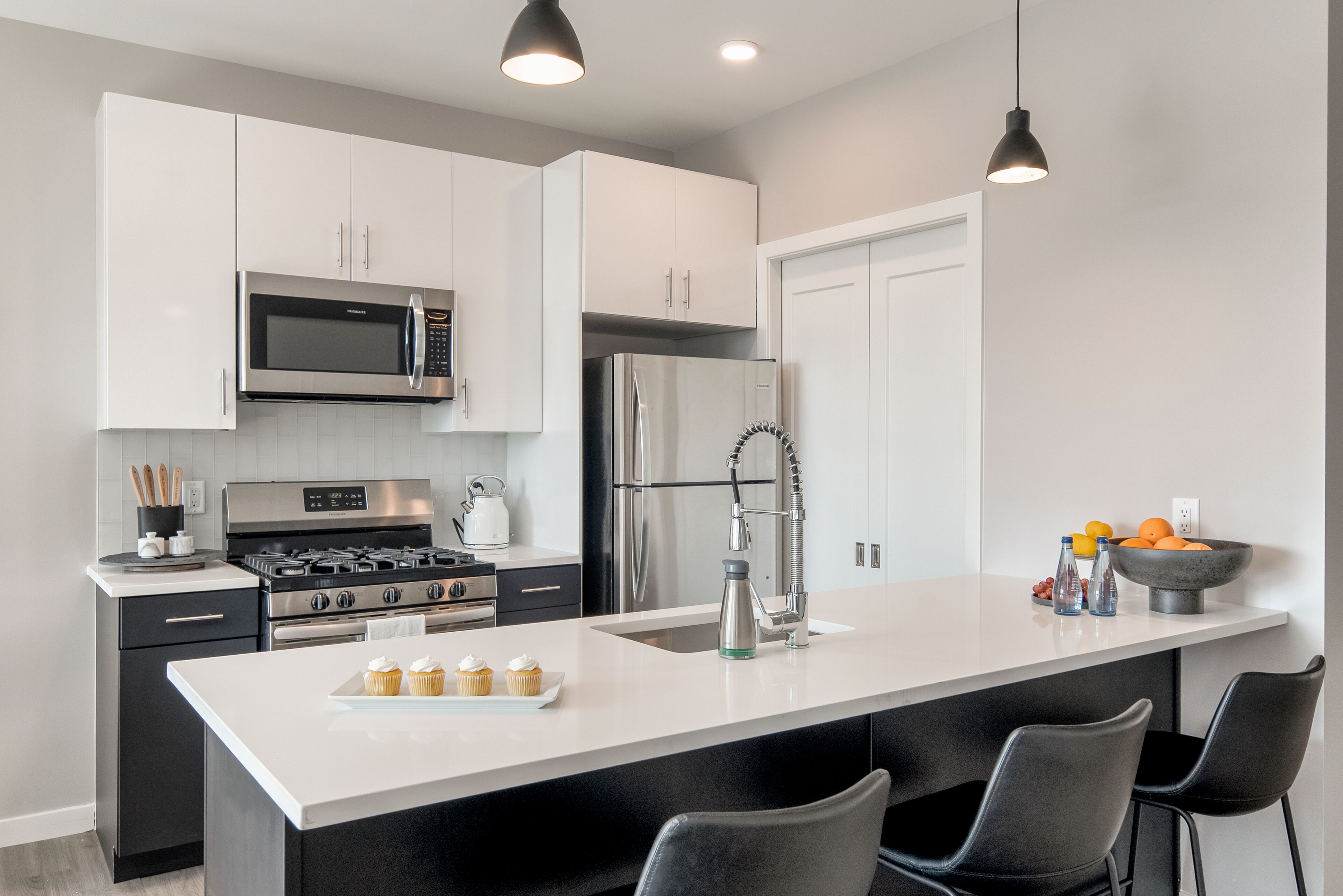 A modern kitchen with white cabinets, stainless steel appliances, a large island with bar seating, and pendant lighting.