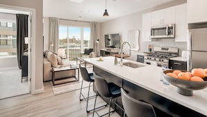 A modern kitchen with a central island, stainless steel appliances, and a large window offering a city view. - Hyatus Luxury Residences City Crossing (New Haven)