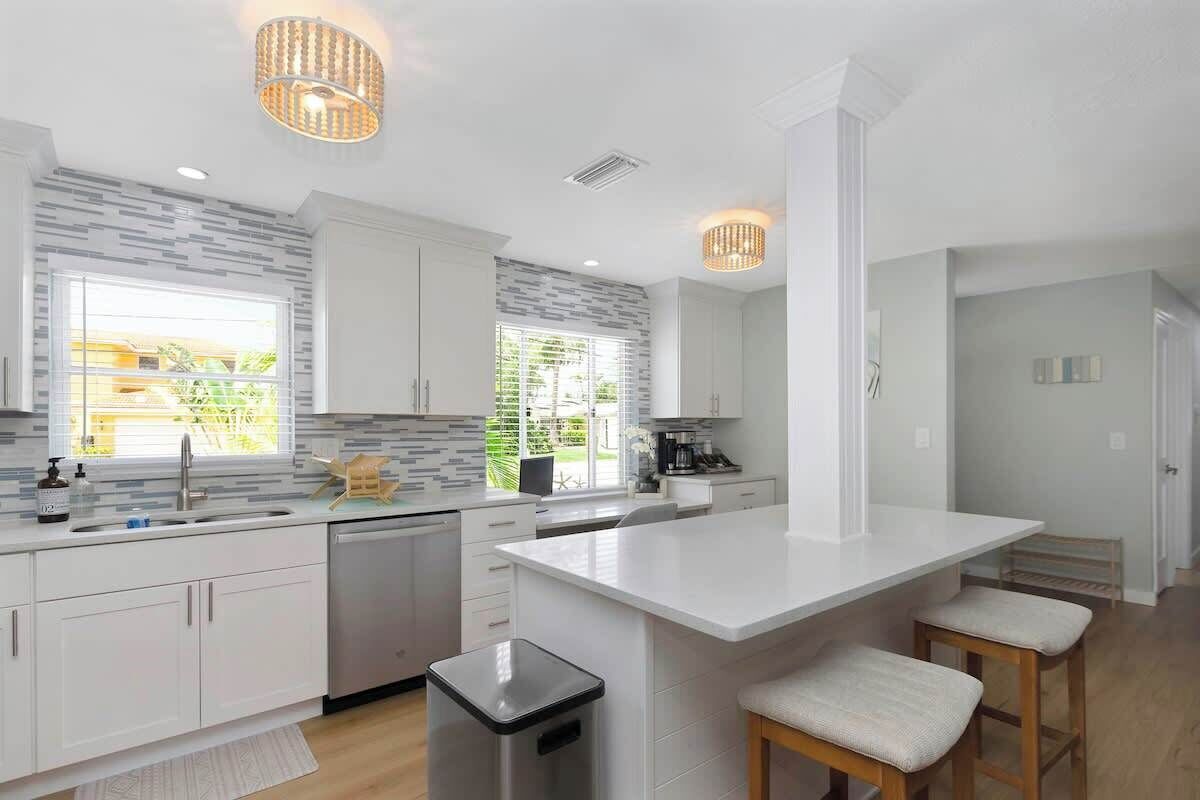 A modern kitchen with white cabinetry, a central island, bar stools, and pendant lighting.