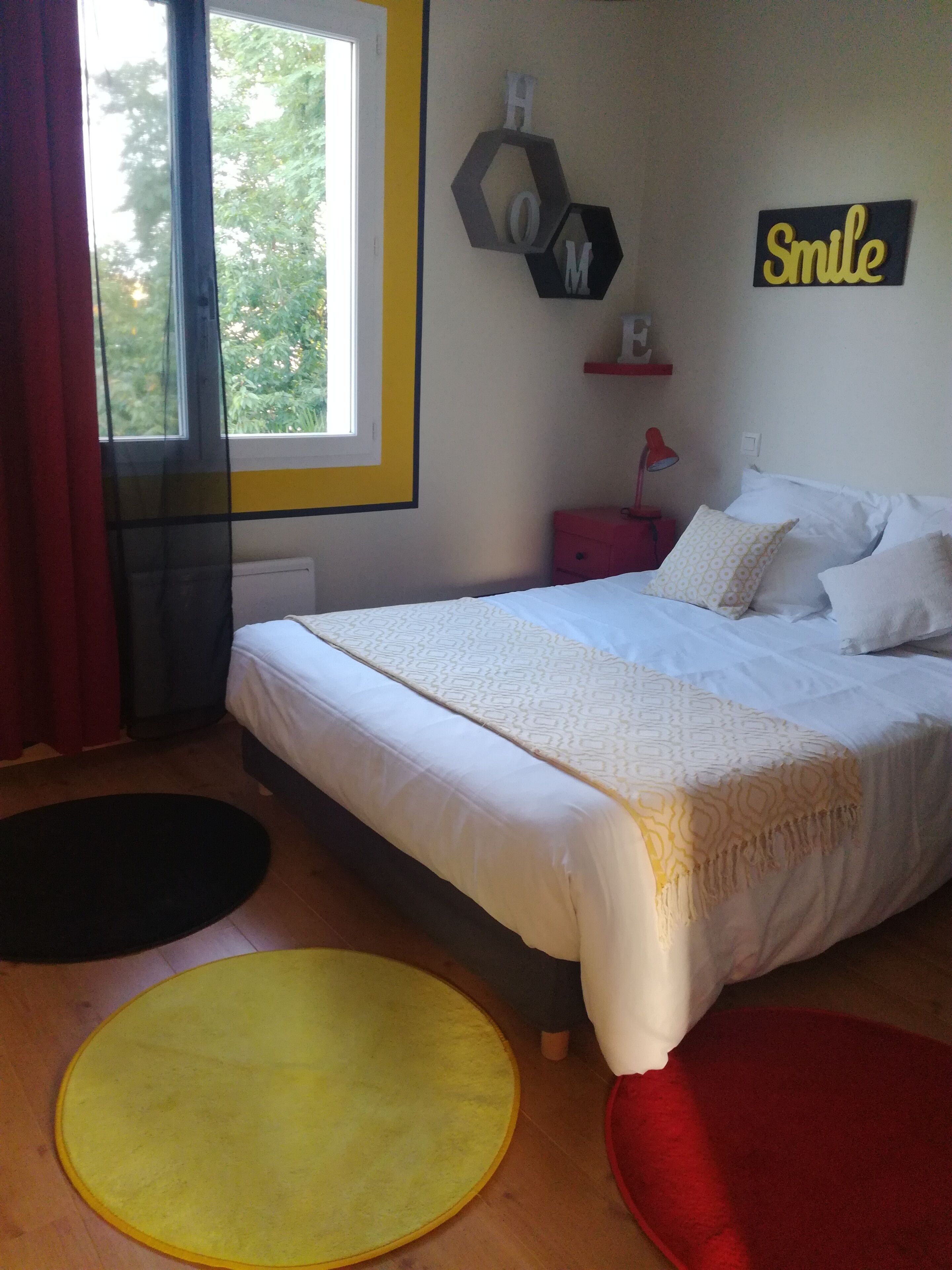 Une chambre à coucher avec un lit, une fenêtre, un élément de décoration murale et une table de chevet rouge.