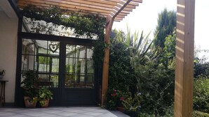 A covered patio area with a tiled floor, a wooden pergola, and a black door with glass panels. - Bassin d'Arcachon family home with swimming pool (LE TEICH)