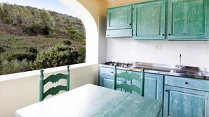 A kitchen with teal cabinets, a white countertop, and a view of a hillside.