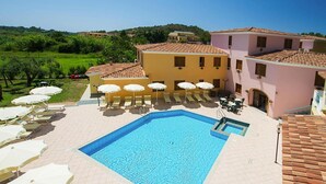 A swimming pool with sun loungers and umbrellas, surrounded by buildings with terracotta roofs.