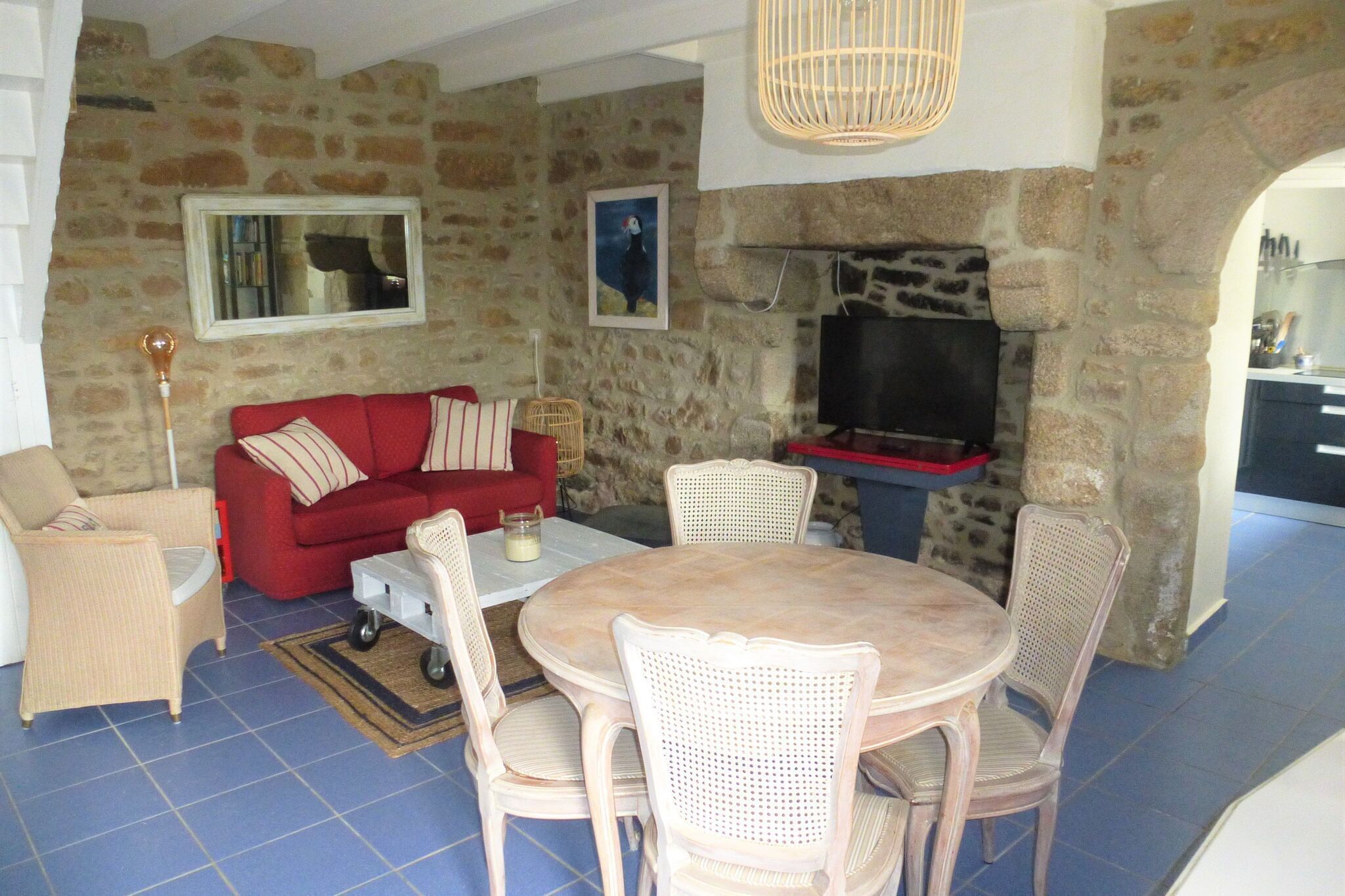 A cozy living room with a stone wall, a red sofa, wicker chairs, a wooden table, and a television.