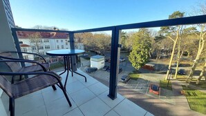 A balcony with a table and chairs, offering a view of a parking area and buildings in the background.