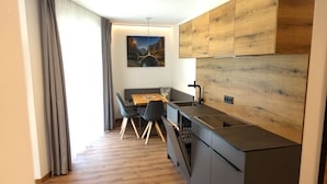 A modern kitchen with a wooden backsplash, a dining area with a table and chairs, and a view of mountains through the window. - Bergzeit Apartments near ski slope (Saalbach-Hinterglemm)