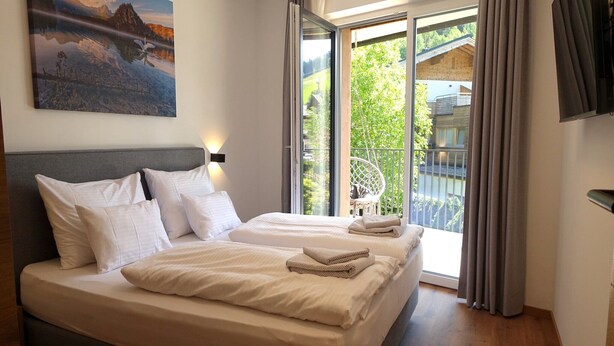 A double bed with white linens, a grey headboard, and a painting above. - Bergzeit Apartments near ski slope (Saalbach-Hinterglemm)