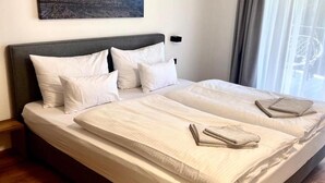 A double bed with white bedding, a headboard, and a bedside table. - Bergzeit Apartments near ski slope (Saalbach-Hinterglemm)