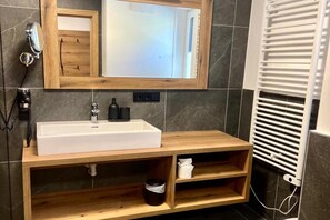 A bathroom with a wooden vanity, a white sink, a mirror, a towel rack, and a towel warmer.