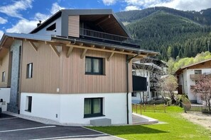 Un edificio moderno de dos pisos con balcón, rodeado de un césped cuidado y con montañas al fondo.