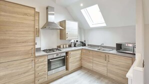 Una cocina moderna con armarios de madera, estufa a gas, horno, microondas y un tragaluz.