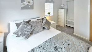 Un dormitorio con cama, mesita de noche, cómoda y ventana con persianas.
