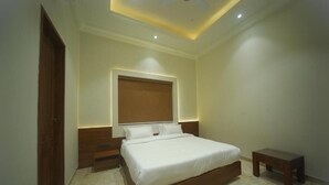 A bedroom with a large bed, a nightstand, a wooden bench, and a ceiling light fixture. - Ratna Vilas Palace (Rajkot)
