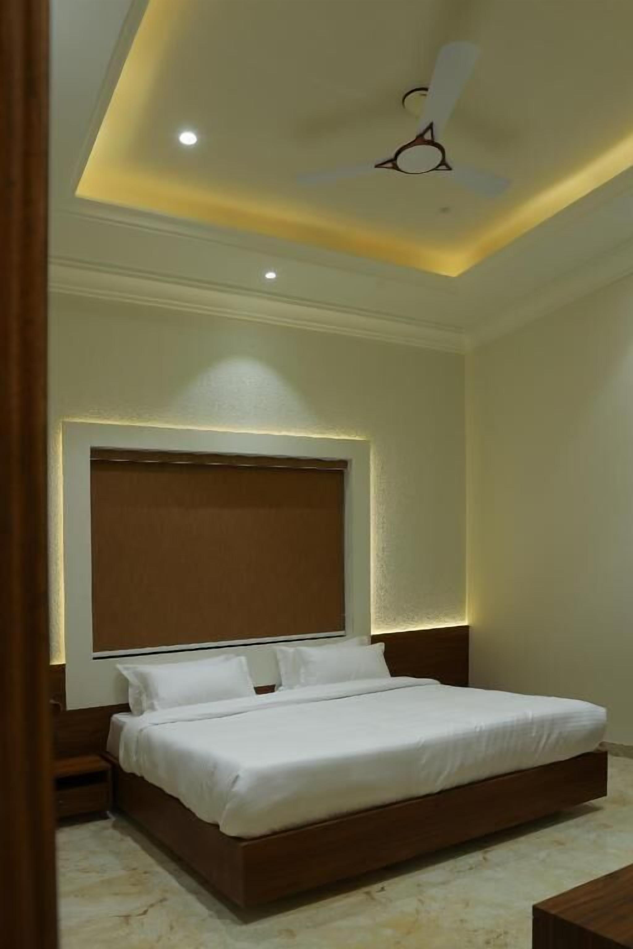 A bedroom with a large bed, a ceiling fan, recessed lighting, and a wooden headboard.