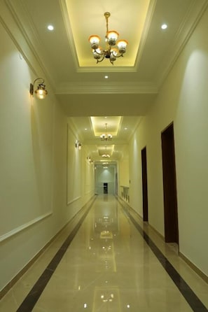 A long, well-lit hallway with a chandelier and wall sconces, leading to a door at the end. - Ratna Vilas Palace (Rajkot)