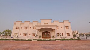 A large, multi-story building with a symmetrical facade, a central entrance with a decorative arch, and a surrounding landscaped area. - Ratna Vilas Palace (Rajkot)