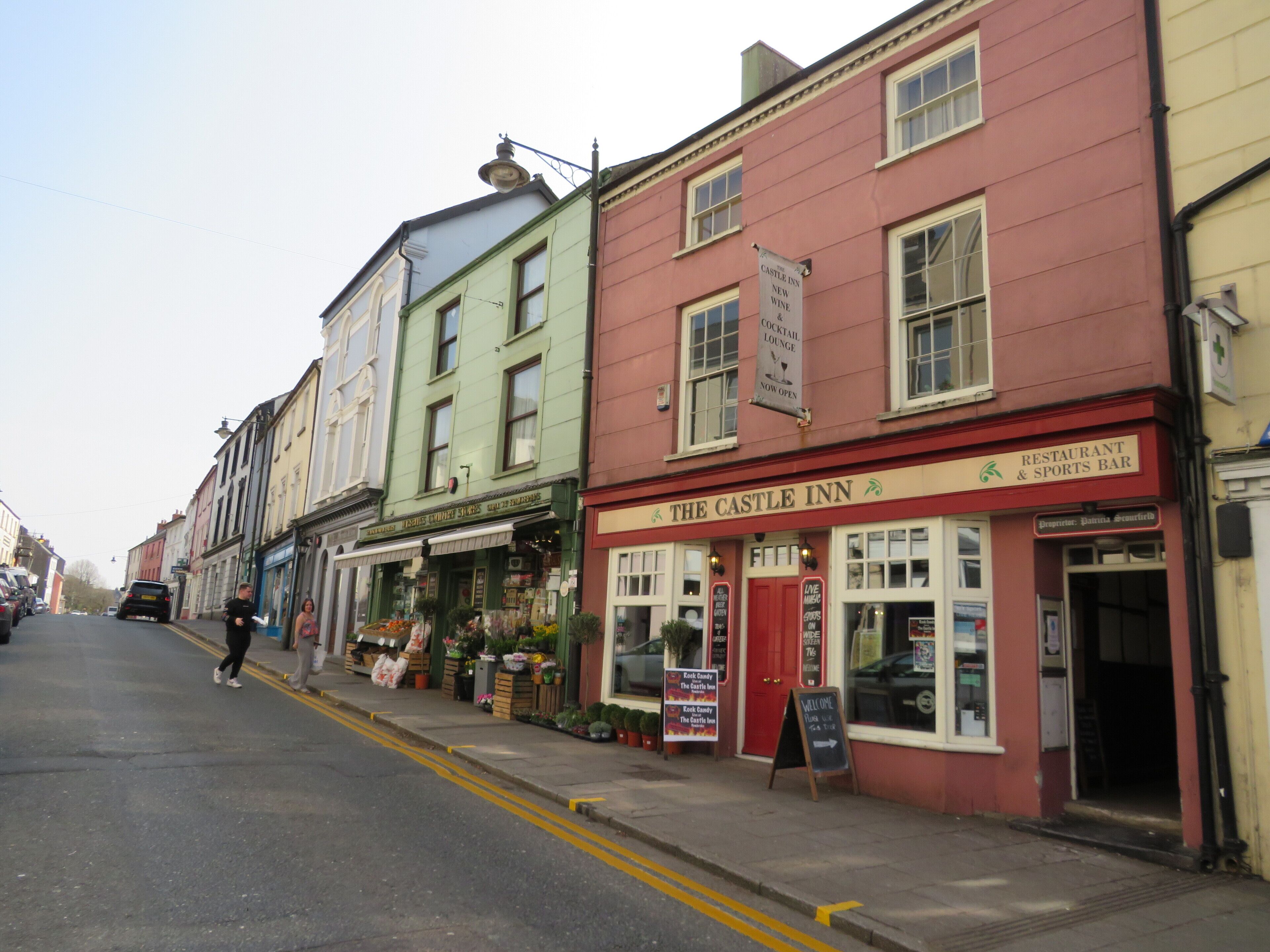 A street view of The Castle Inn, a restaurant and sports bar with a red facade and a signboard advertising a cocktail lounge.