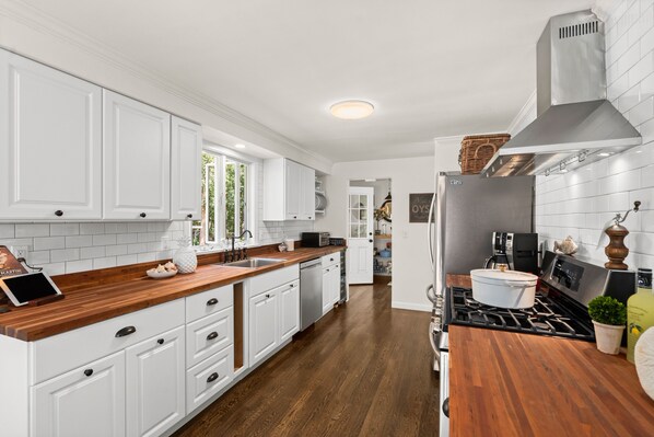 A modern kitchen with white cabinetry, a wooden countertop, and a stainless steel range hood. - Wellfleet Beach House (Wellfleet)